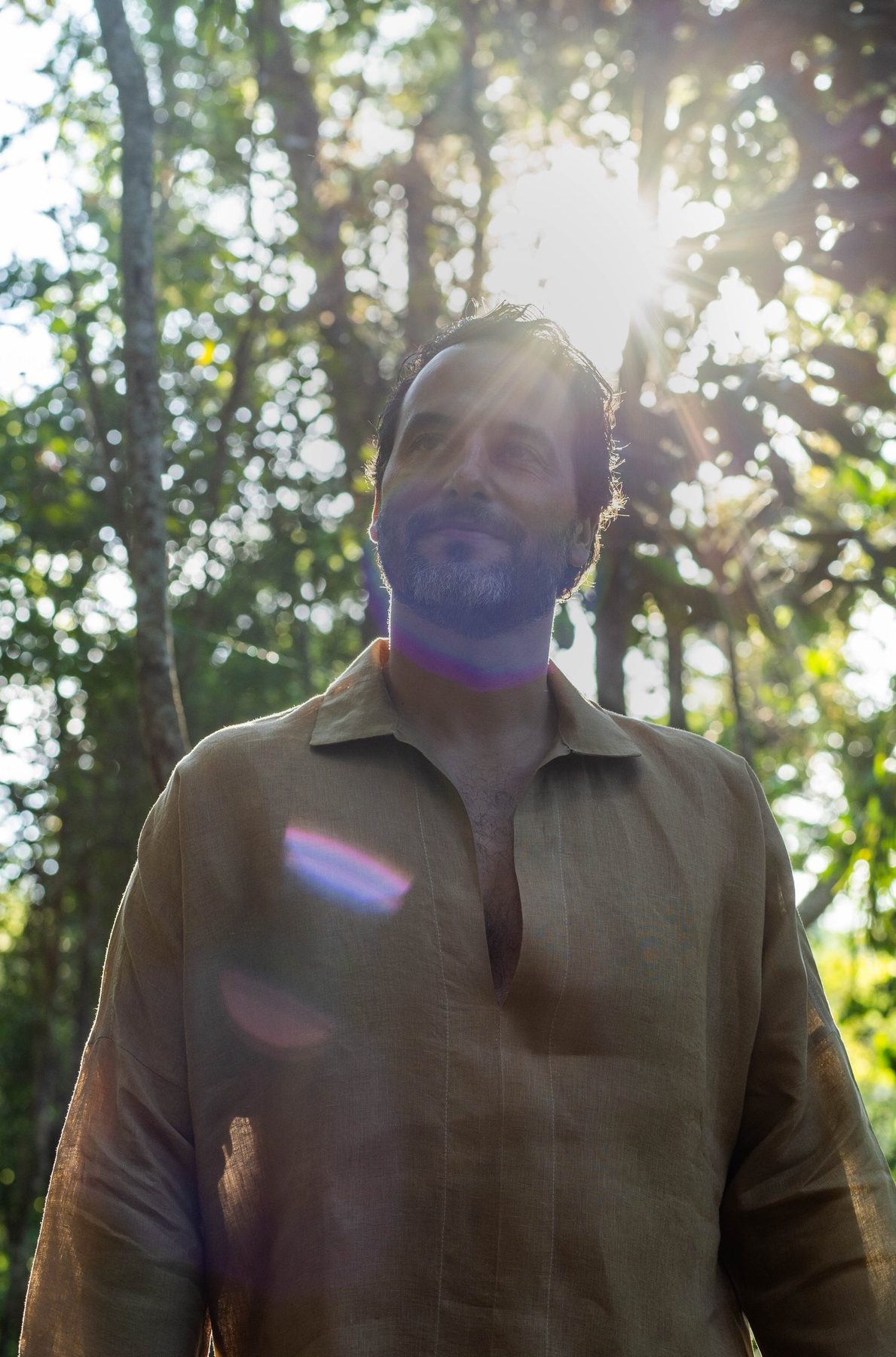 Rael Luz na mata, sorrindo, com o sol atrás da cabeça